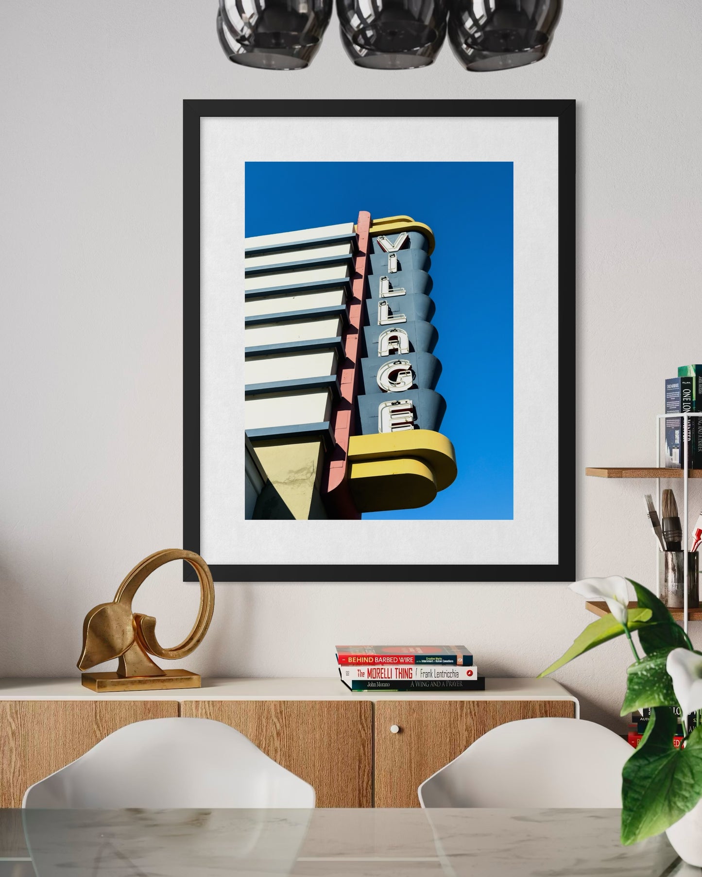 The "Village Theater on Coronado Island - Fine Art Print" by Leslie Brashear Photography is displayed above a light wood sideboard with decor, books, and white chairs in the foreground.