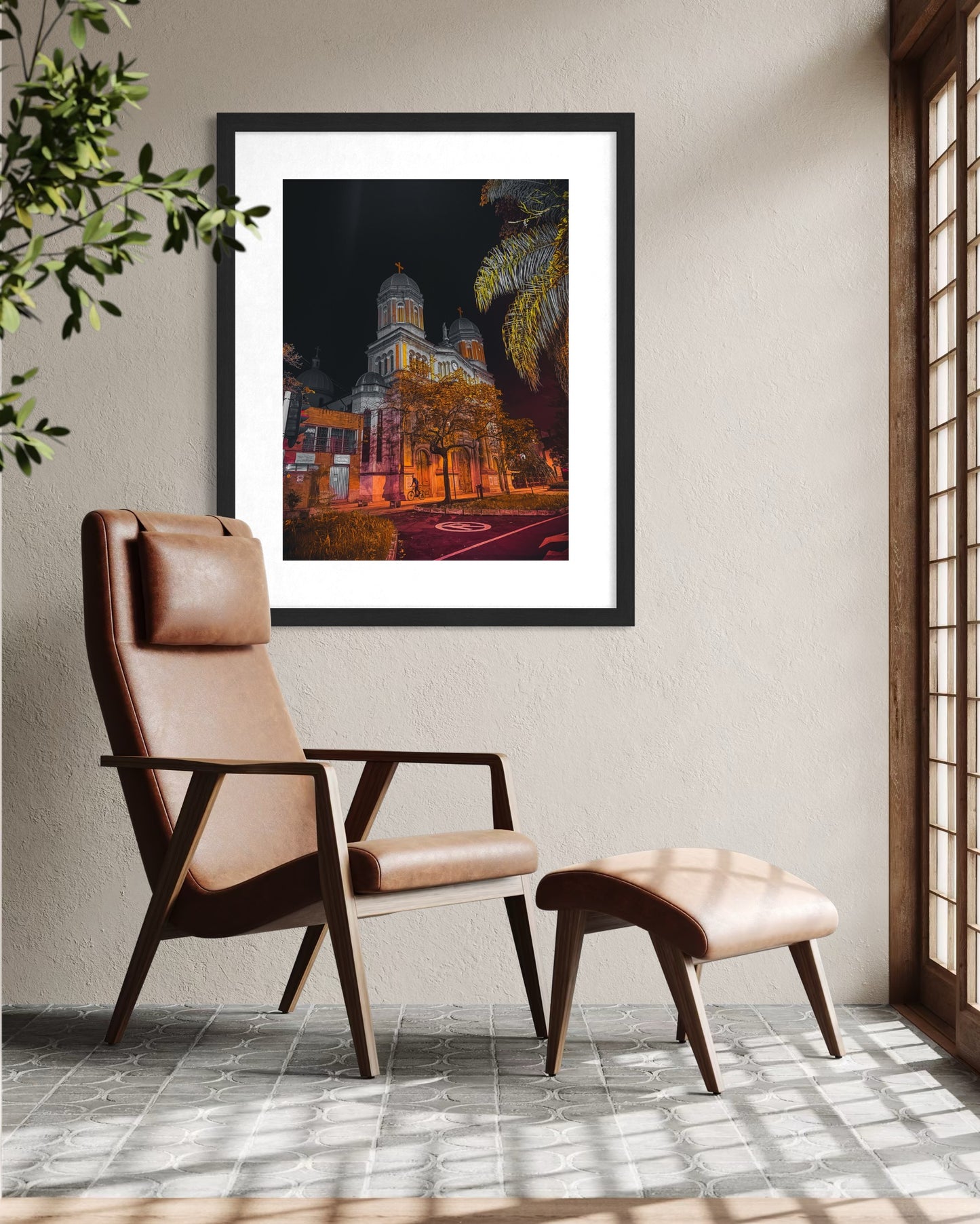 A modern leather chair and ottoman sit in a sunlit room, with "Church at Night - Fine Art Print" by Leslie Brashear Photography, featuring an illuminated building at night, framed on the wall.
