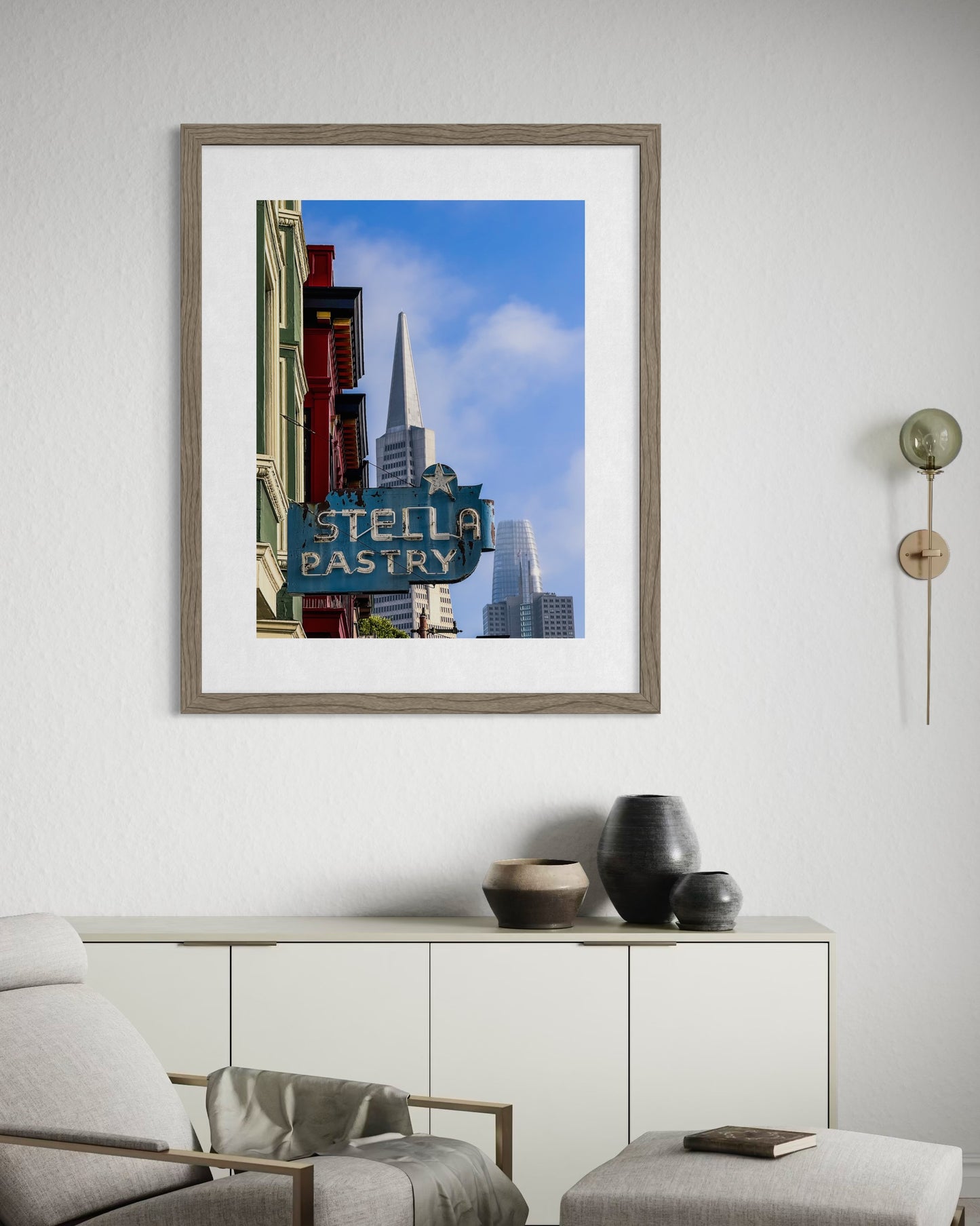 The Retro Stella Pastry Sign - Fine Art Print by Leslie Brashear Photography is displayed above a beige cabinet with vases, showing the iconic North Beach sign and Transamerica Pyramid on a white wall in a modern living room.