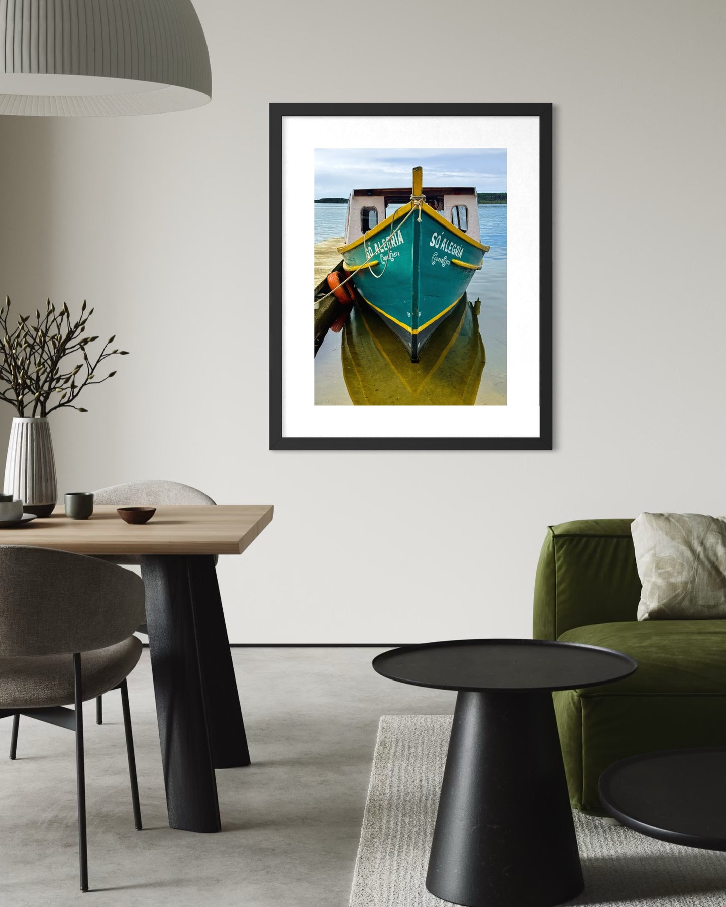 A modern living room features neutral-toned furniture and "So Alegria - Fine Art Print" by Leslie Brashear Photography—a framed photo of a green and yellow boat on calm water—adding Florianópolis charm to the space.