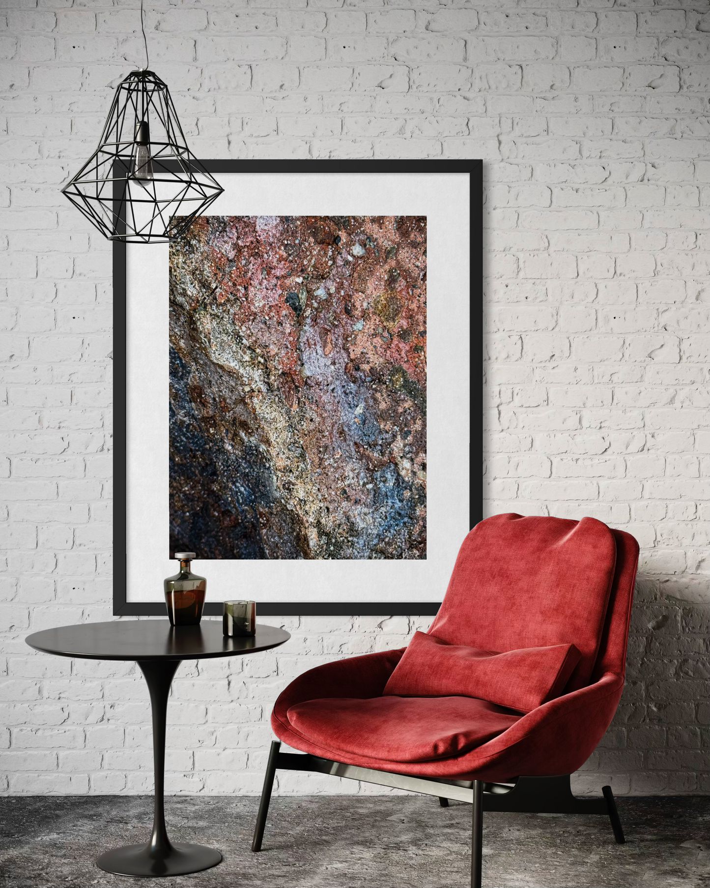 A modern interior with a red armchair, round black table, pendant light, and Leslie Brashear Photography’s "Cliffside Colors and Textures" artwork framed on a white brick wall.