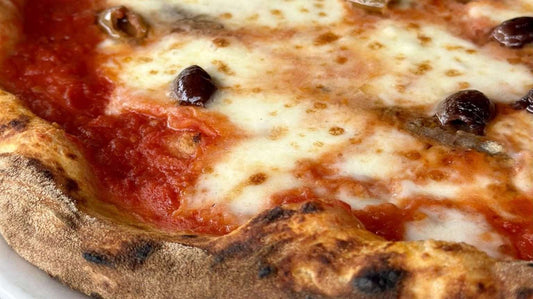 Close-up of a Napoletano style pizza while visiting Milan with a thick crust, topped with melted cheese, tomato sauce, and olives.