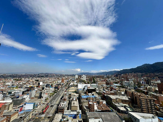 Aerial view of a densely built Bogota with a railway, surrounded by mountains under a blue sky