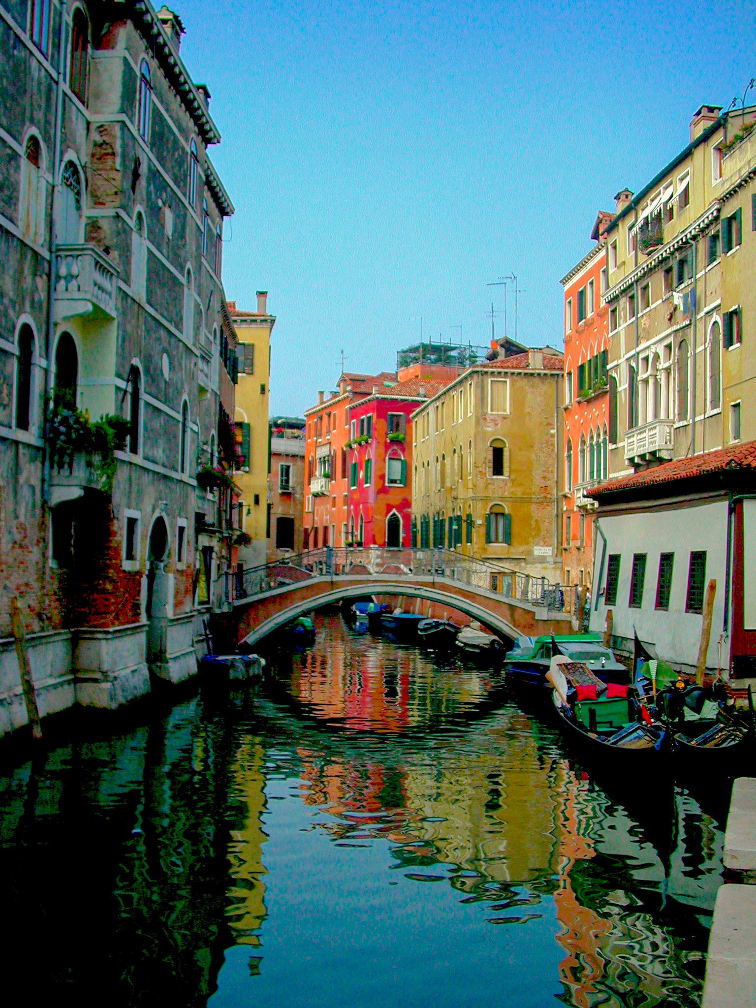 Quiet Venice Canal - Fine Art Print features a narrow canal framed by colorful Venetian buildings, a charming arched stone bridge, and boats moored along calm waters—perfect for lovers of serene photography and classic architecture.