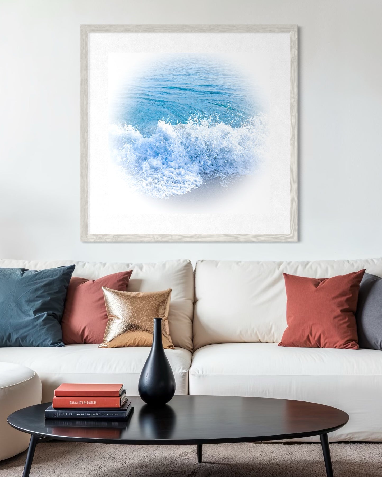 A modern living room with a white sofa, colorful throw pillows, a black oval coffee table, and "Gentle Ocean Waves - Fine Art Print" by Leslie Brashear Photography displayed on the wall.