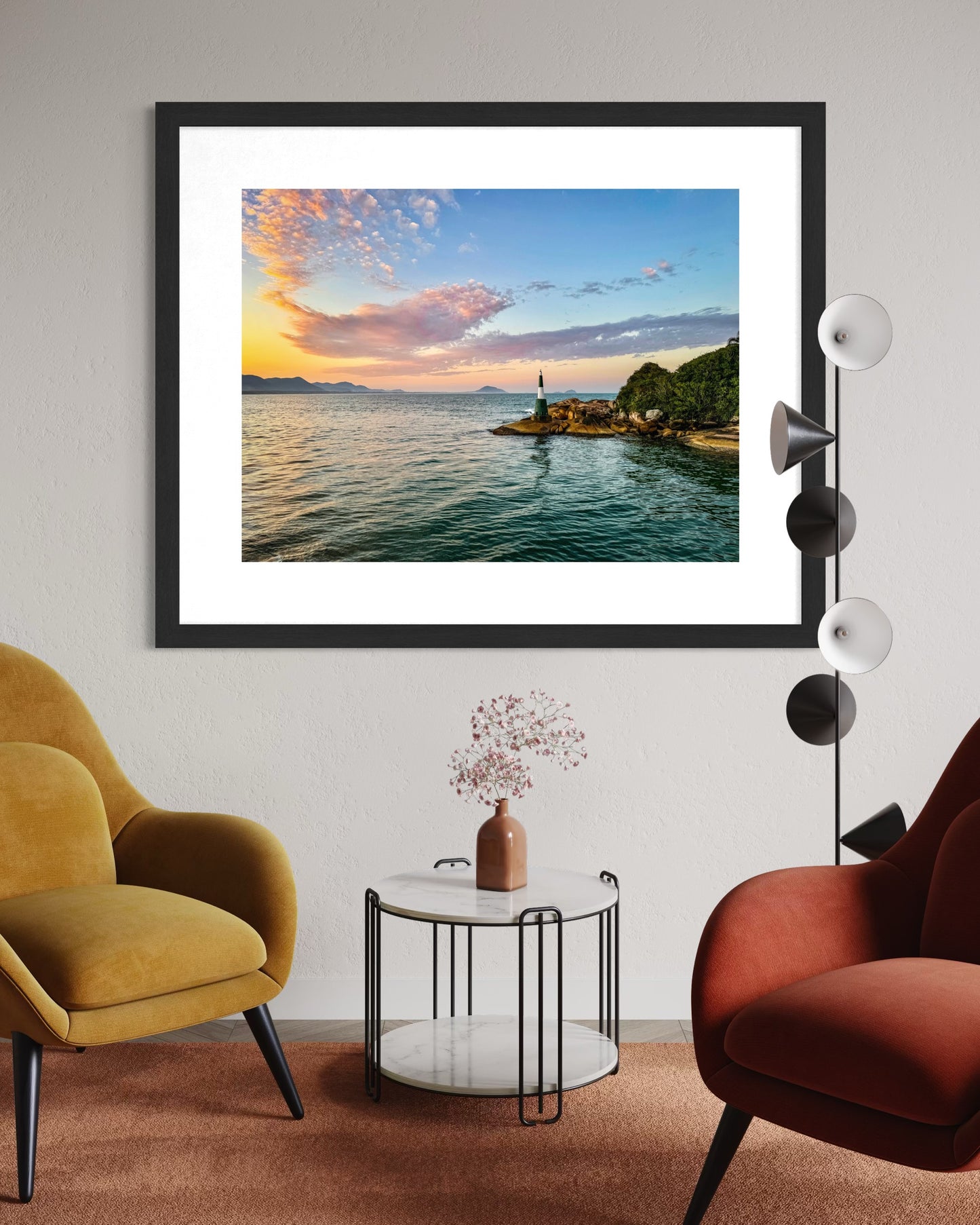 A modern living room with mustard and rust chairs, a round table, and Coastal Sunset - Fine Art Print by Leslie Brashear Photography featuring the Florianópolis lighthouse on the wall.
