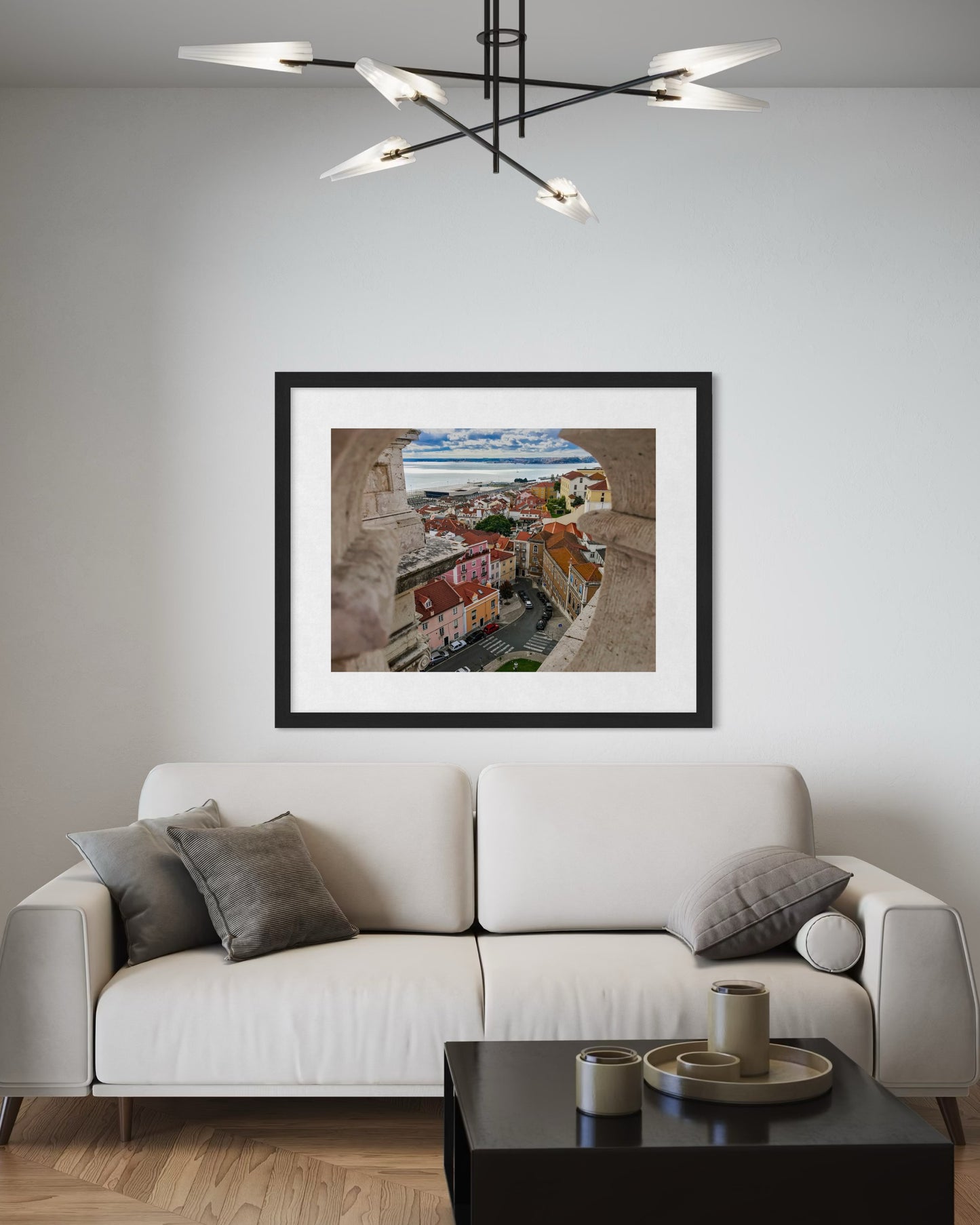 A modern living room features a white sofa, gray cushions, and the "Lisbon - Fine Art Print" by Leslie Brashear Photography on the wall; a contemporary chandelier hangs above.