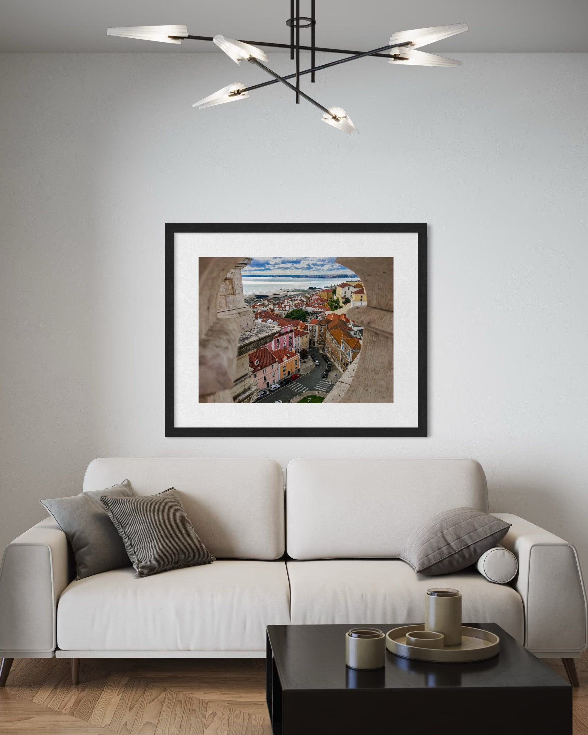 A modern living room features a white sofa, gray cushions, and the "Lisbon - Fine Art Print" by Leslie Brashear Photography on the wall; a contemporary chandelier hangs above.