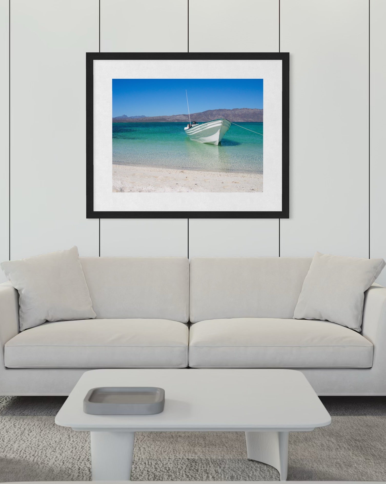 A white sofa and table in a modern living room, with "Peaceful Boat - Fine Art Print" by Leslie Brashear Photography—a beach and blue water scene from Loreto, Mexico—evoking the minimalist Sea of Cortez landscape, hanging above.
