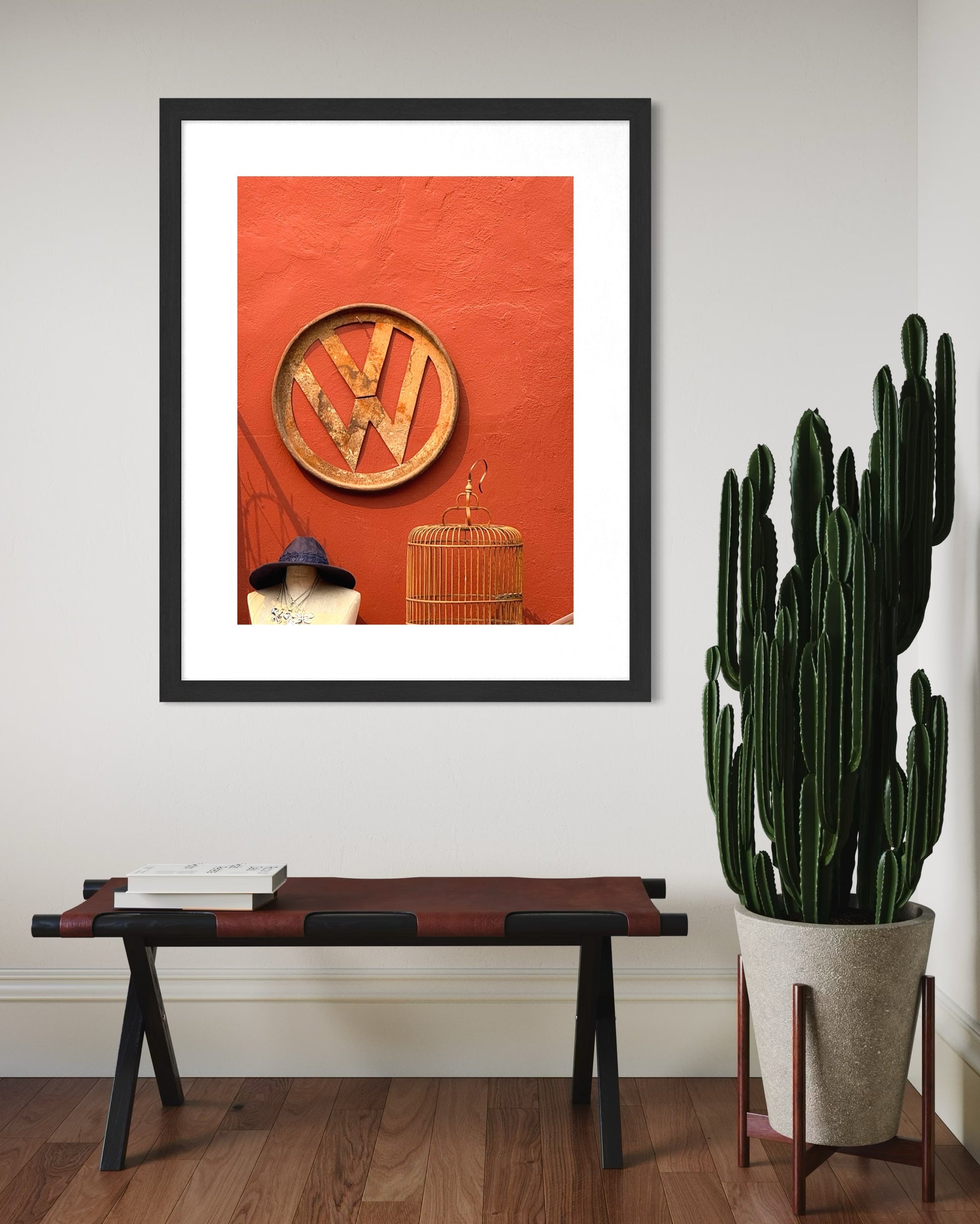 A framed VW Sign for Sale - Fine Art Print by Leslie Brashear Photography decorates the wall, featuring rustic style. Below, a bench with books and retro accents is complemented by a potted cactus nearby.