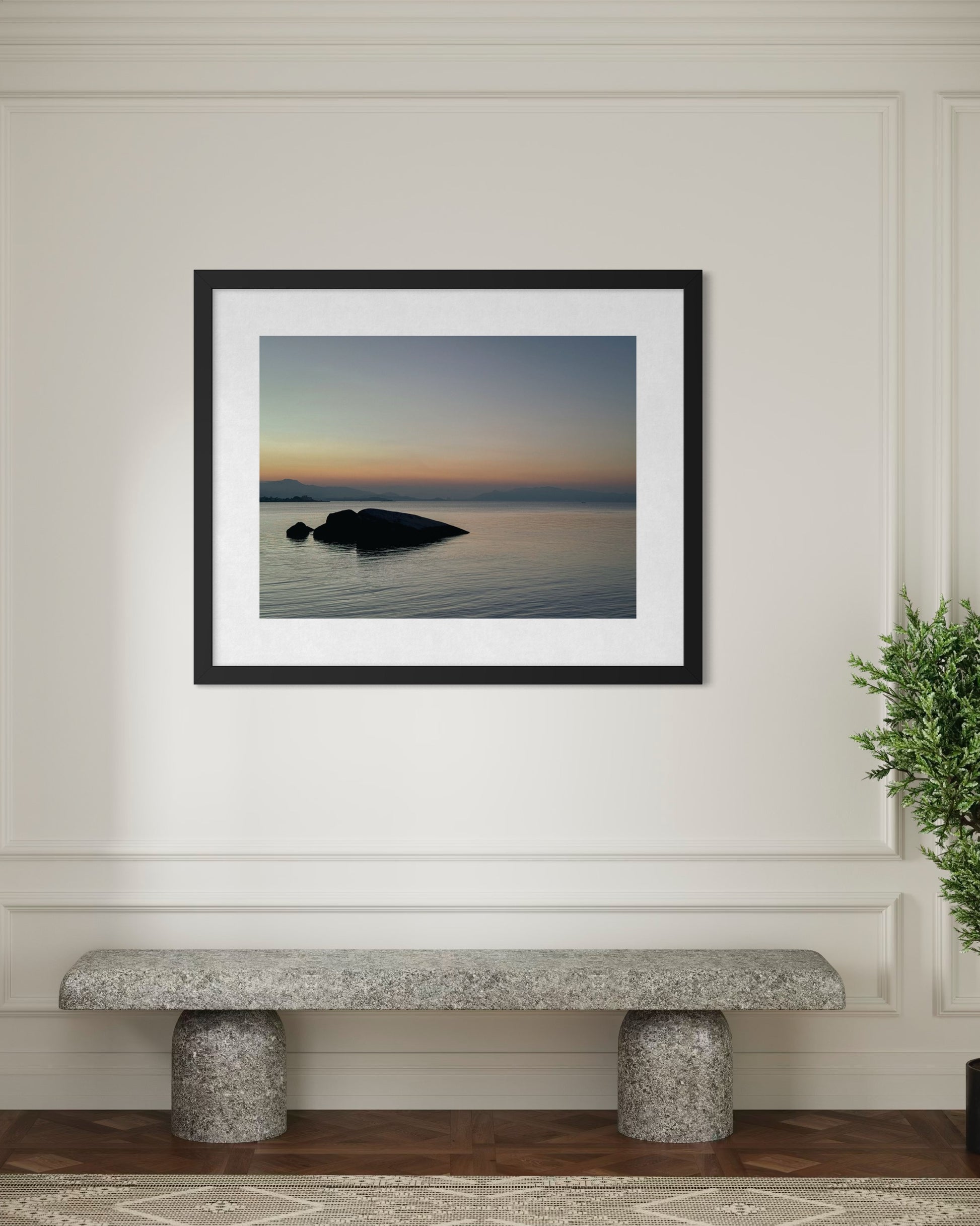 Twilight Serenity Over Still Waters - Fine Art Print by Leslie Brashear Photography hangs above a stone bench with a green plant, bringing the tranquil beauty of Florianópolis dusk seascapes to your space.