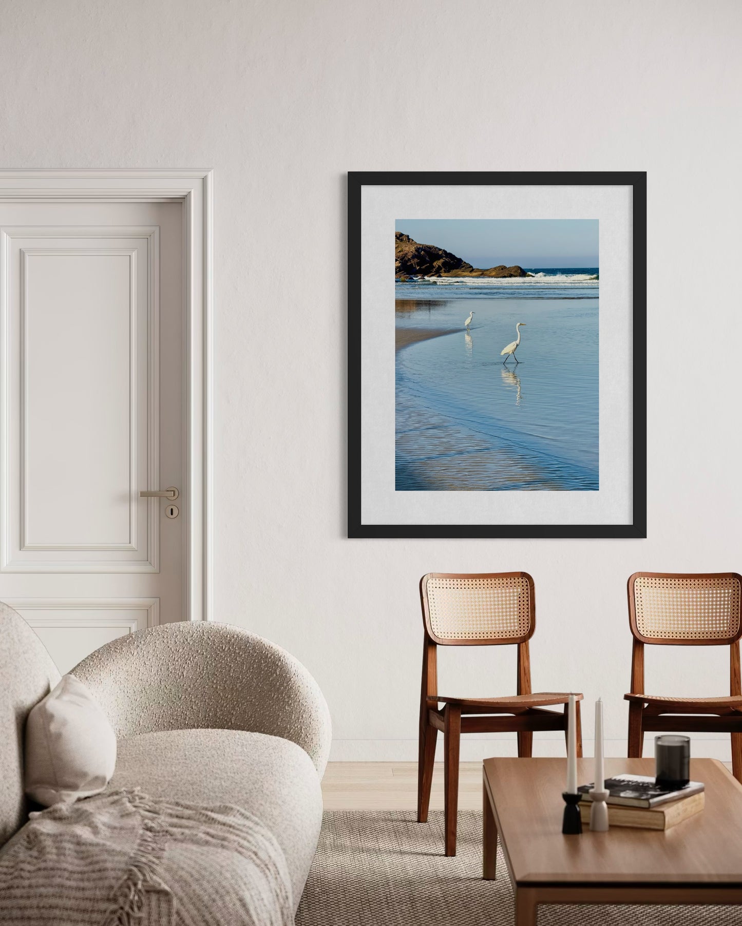 The "Egrets Wading in Shallow Water - Fine Art Print" by Leslie Brashear Photography is displayed above two wooden chairs on a white wall, creating a modern living room focal point.