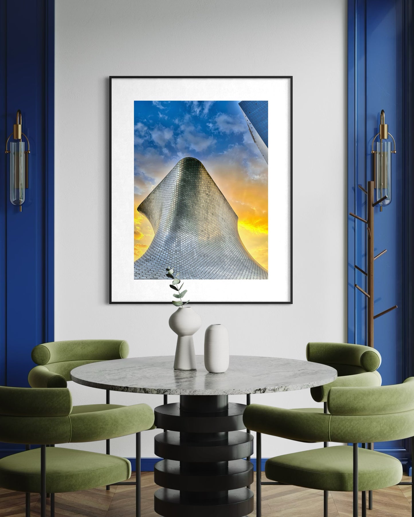 A modern dining area with a round marble table, four green chairs, blue accent walls, and "Soumaya Museum at Sunset - Fine Art Print" by Leslie Brashear Photography—a tribute to Mexico City's iconic architecture.