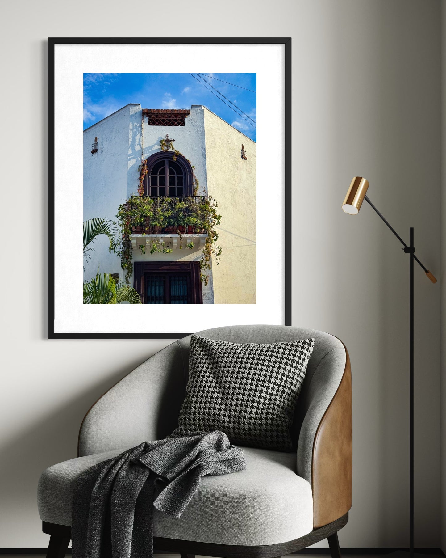 The "Charming Corner Balcony - Fine Art Print" by Leslie Brashear Photography, inspired by Guadalajara architecture, hangs above a modern armchair and floor lamp in a minimalist room.
