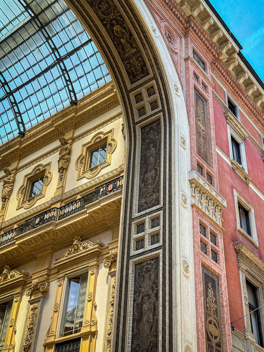 The Ornate Architectural Detail at Galleria Vittorio Emanuele II Fine Art Print by Leslie Brashear Photography highlights Milan’s grandeur with its arched glass roof, intricate columns, gold accents, and red and cream walls.