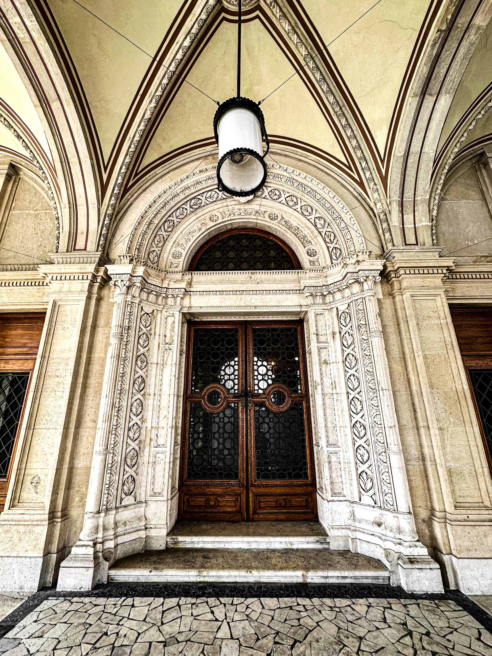 Doorway to the Opera - Fine Art Print by Leslie Brashear Photography captures an ornate arched wooden doorway with carved details, columns, and a stone facade beneath a vaulted ceiling with lantern, evoking Gothic elegance.