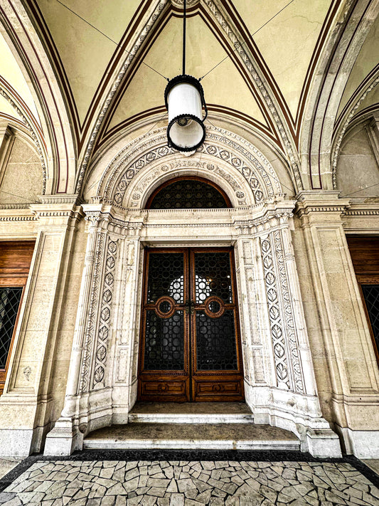 Doorway to the Opera - Fine Art Print by Leslie Brashear Photography captures an ornate arched wooden doorway with carved details, columns, and a stone facade beneath a vaulted ceiling with lantern, evoking Gothic elegance.