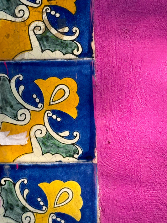 The "Vibrant Tiles and Bright Pink Wall - Fine Art Print" by Leslie Brashear Photography showcases three floral tiles in blue, yellow, and green beside a textured, vivid pink stucco wall.