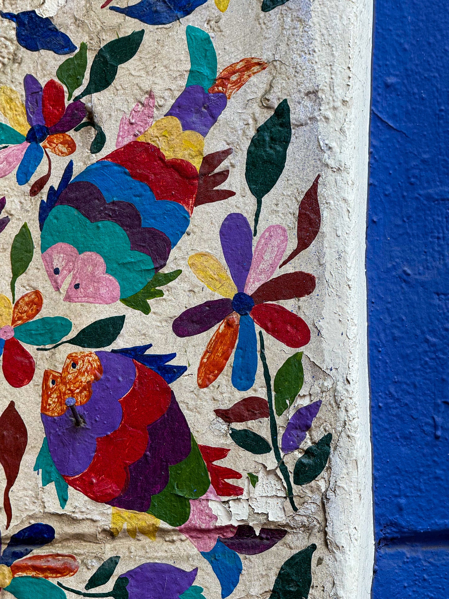 Vibrant Wall Art in Puebla - Fine Art Print by Leslie Brashear Photography features a colorful mural of stylized birds and flowers inspired by Mexican folk art on a textured white wall with a blue section on the right.