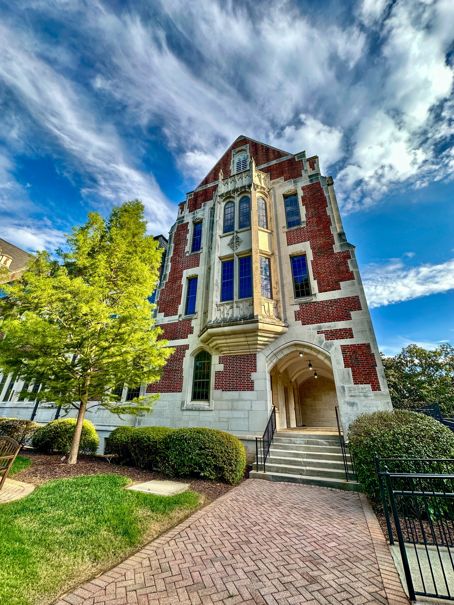 Captured by Leslie Brashear Photography, this Agnes Scott College academic hall showcases red brick Gothic Revival architecture with an arched entrance, large windows, and landscaped grounds under a partly cloudy sky.