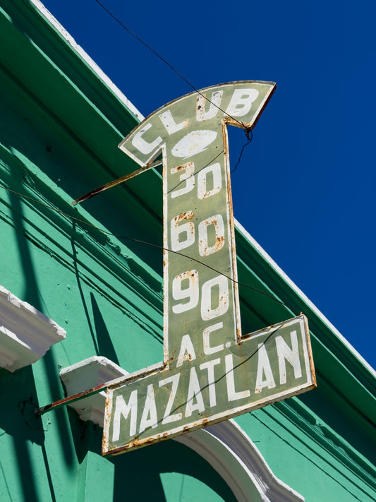 The Retro Club Sign in Mazatlan by Leslie Brashear Photography features a vintage metallic “CLUB 30 60 90 A.C. MAZATLAN” design on a green building, bringing nostalgic charm to Central Mazatlán under a clear blue sky.
