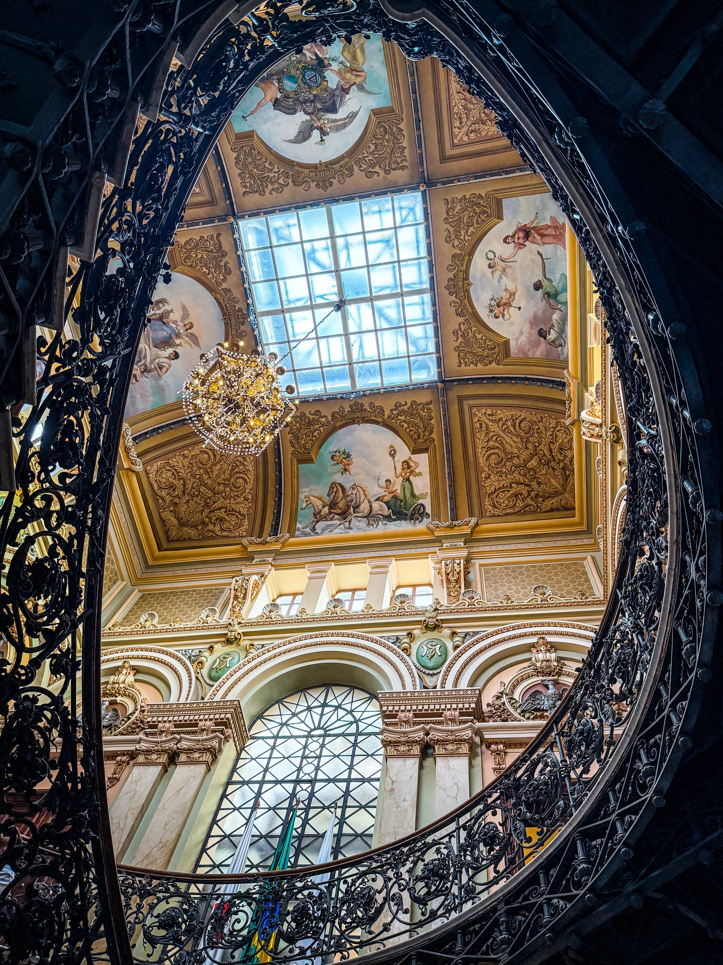 Opulent Elegance Under the Skylight – Fine Art Print by Leslie Brashear Photography showcases an ornate Brazilian ceiling with classical paintings, a glass skylight, chandelier, and decorative iron railing at Palácio da Liberdade.