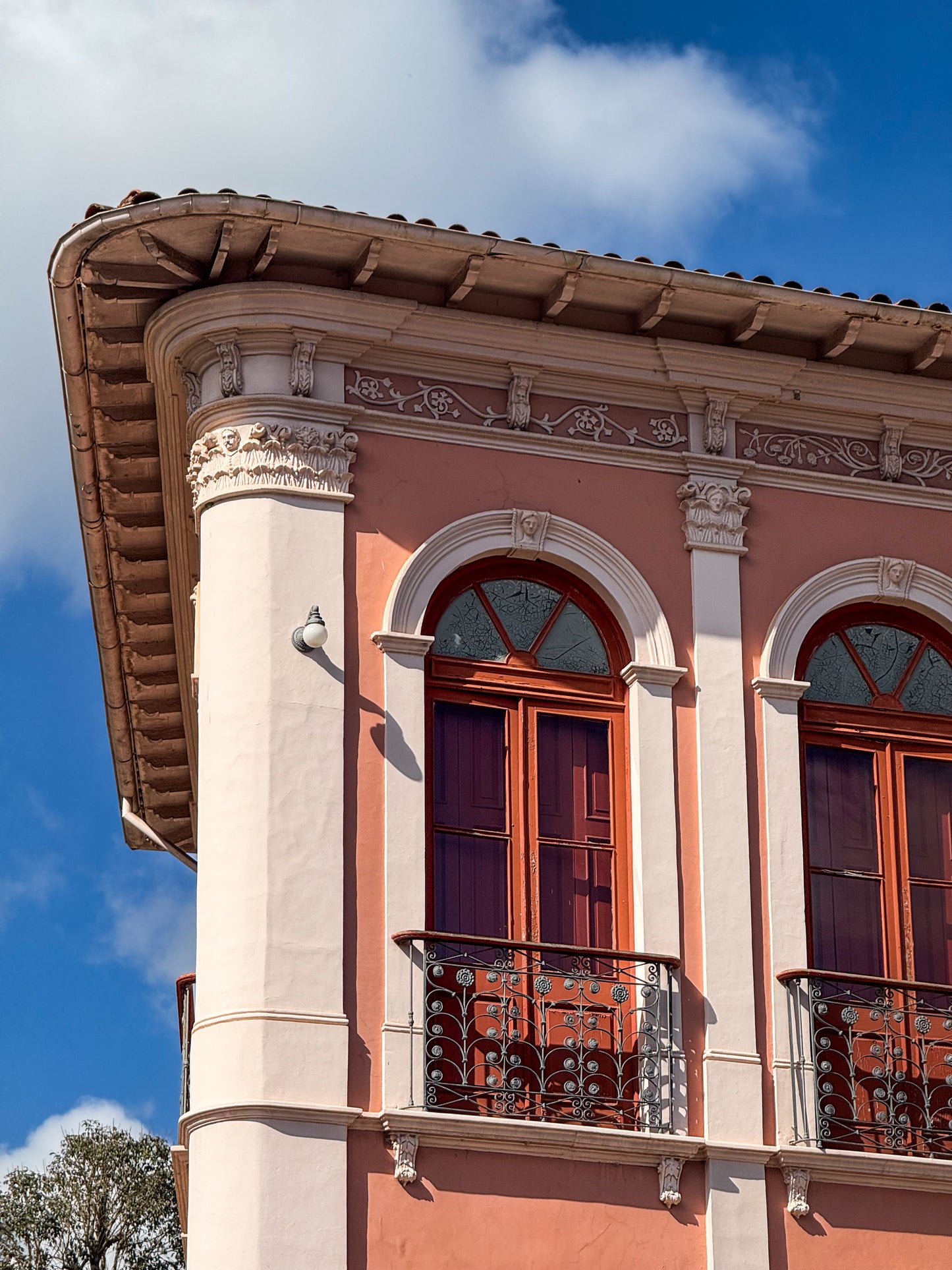 Corner view of Ornate Balcony with Arched Windows by Leslie Brashear Photography, featuring Ouro Preto architecture, arched wooden windows, white trim, wrought iron balcony, and tiled roof beneath a blue sky.