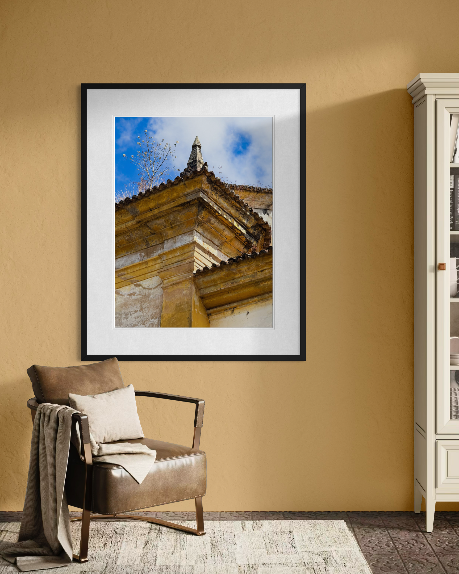 Weathered Church Corner with Rooftop Tree" by Leslie Brashear Photography hangs on a tan wall above a leather chair with a blanket, beside a white cabinet.